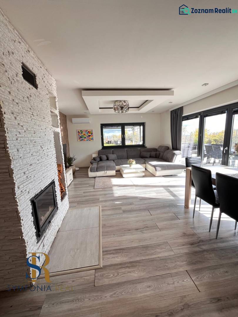 Interiér rodinného domu s pohovkou, krbem a podlahou s dřevěným dekorem.