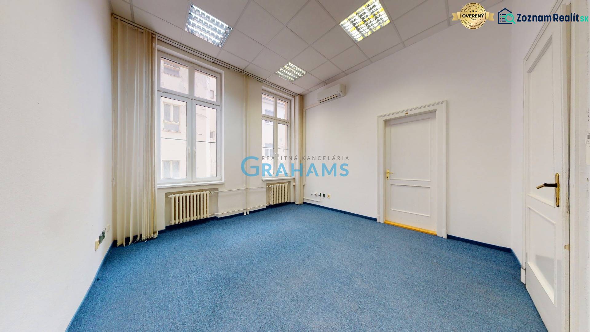 Kanceláře s kazetovým stropem, modrým kobercem a velkými okny.