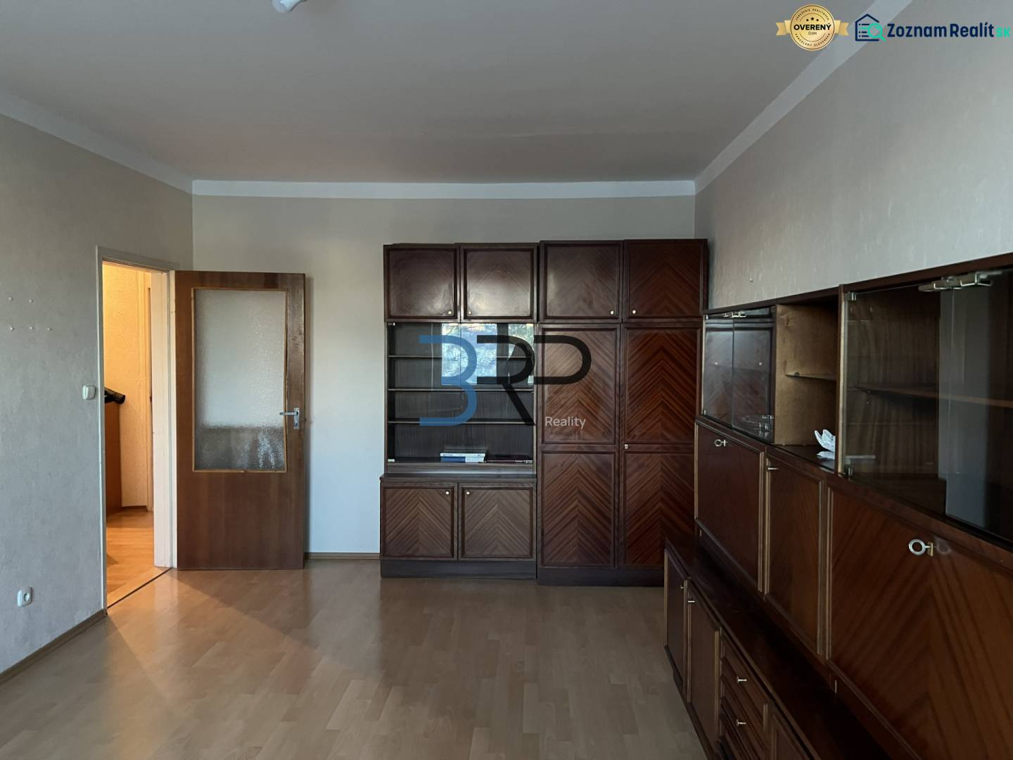 Obývací pokoj v 2pokojovém bytě s velkou dřevěnou obývací sestavou a podlahou s dřevěným dekorem.