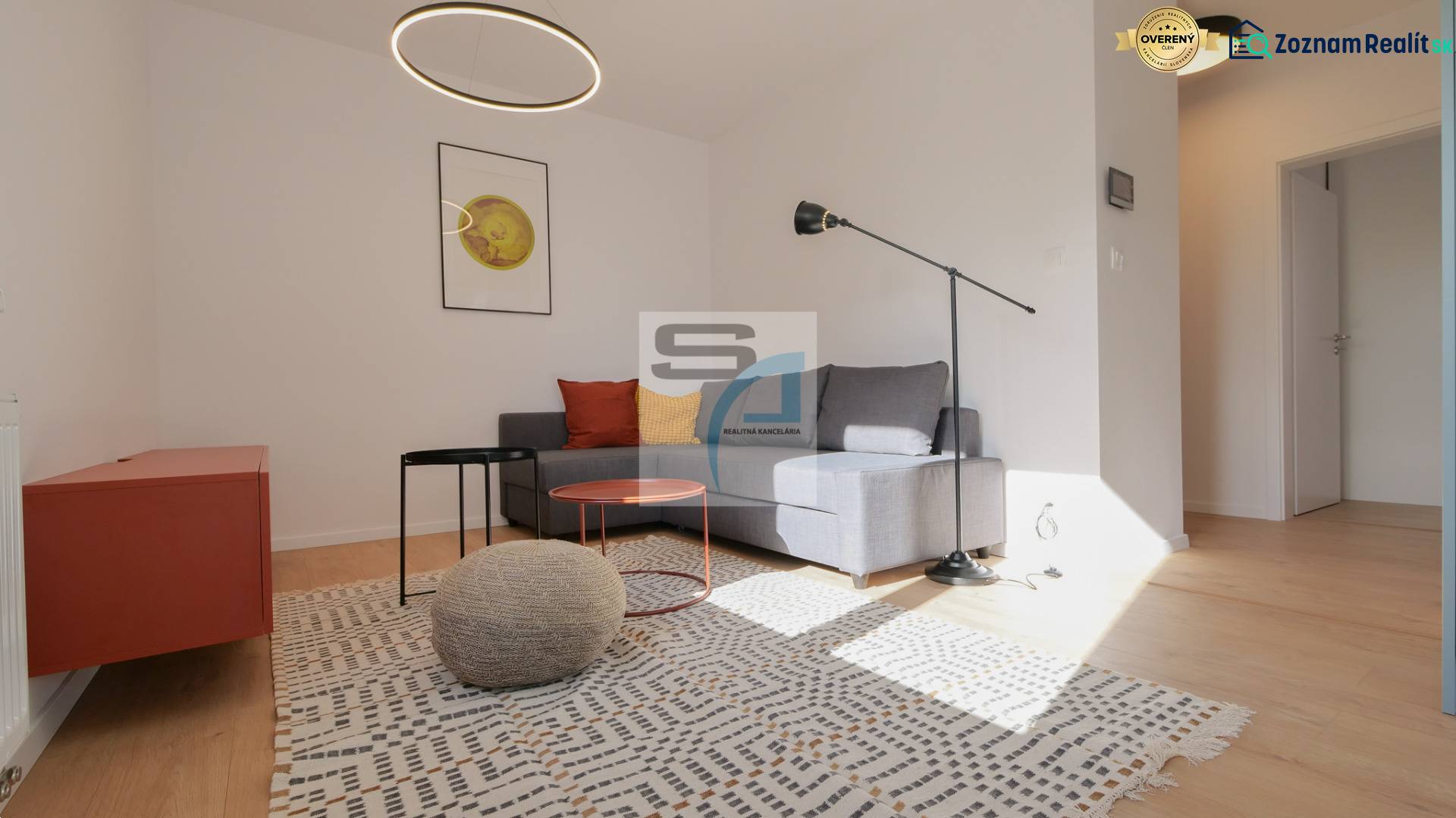 Obývací pokoj v 2-pokojovém bytě s podlahou s dřevěným dekorem, šedou sedačkou a moderním osvětlením.
