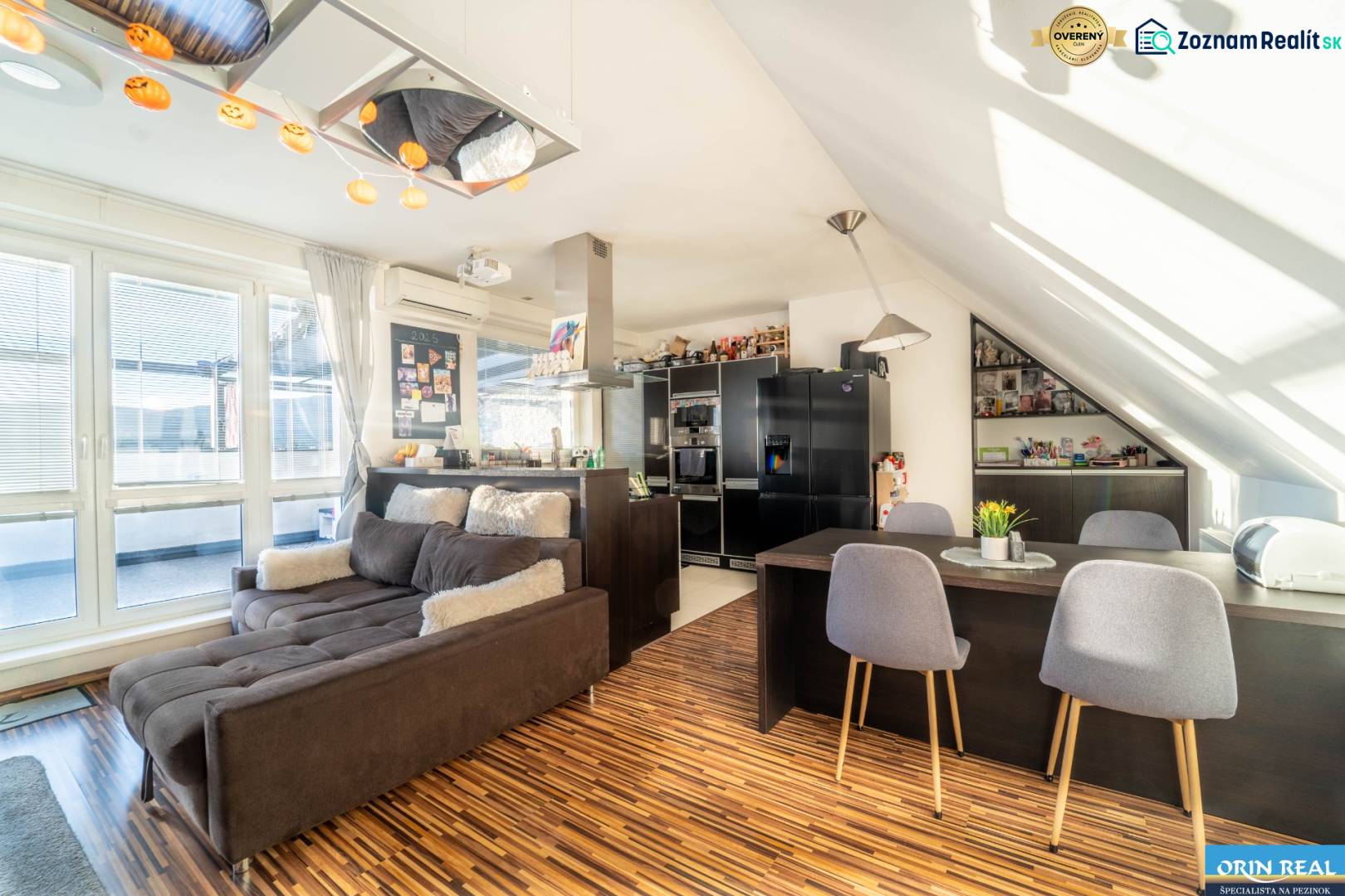 Obývací pokoj s kuchyní ve 2-pokojovém bytě s podlahou s dřevěným dekorem a pohodlnou sedačkou.