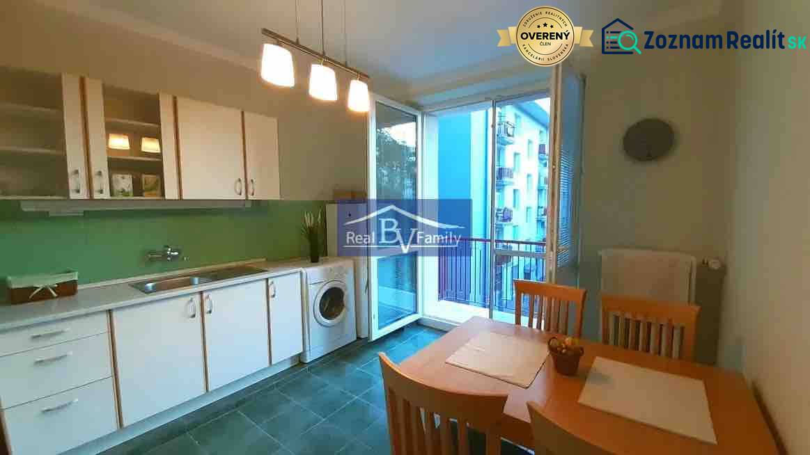 Kuchyně v 2pokojovém bytě s bílými skříňkami, jídelním stolem a balkónem.