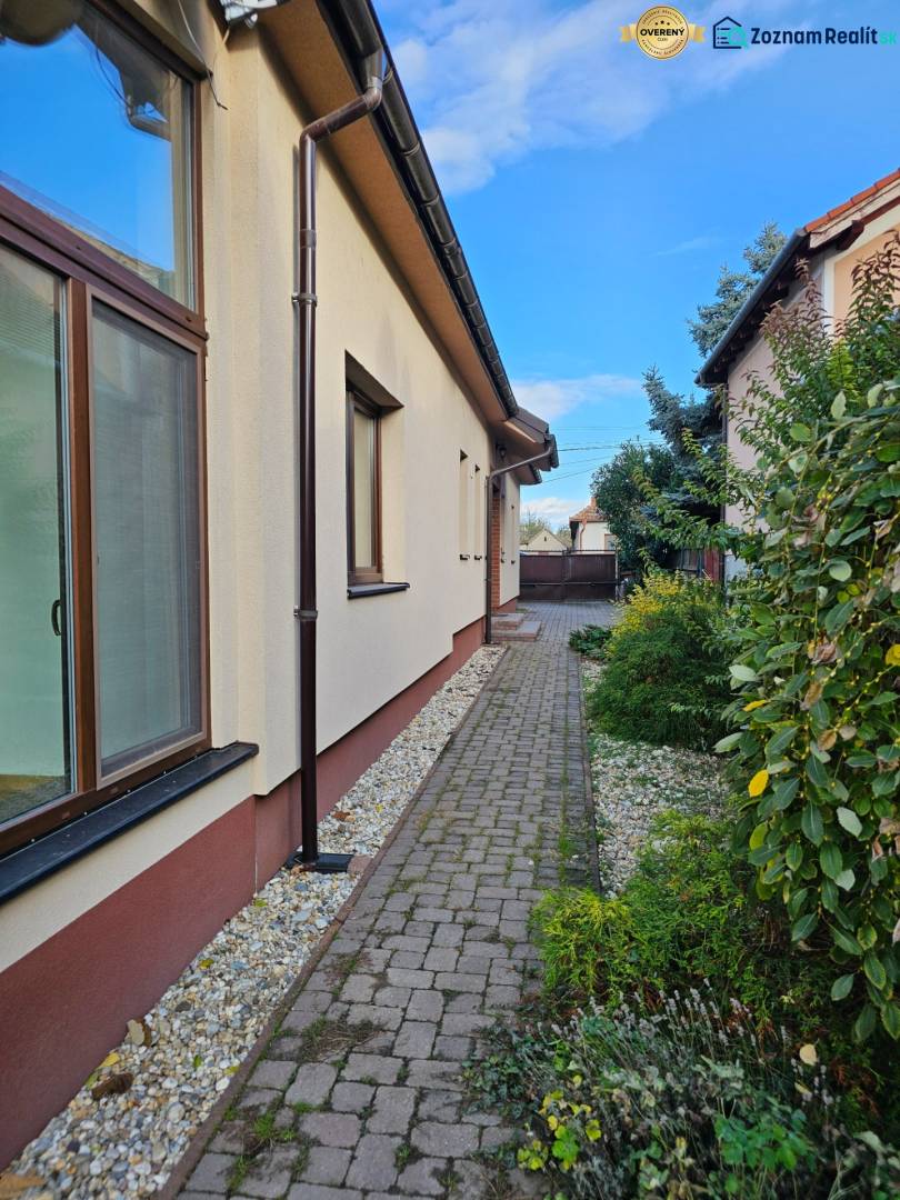 Pohled na boční část rodinného domu v Štúrově ulici ve Vráblech s dlážděným chodníkem.