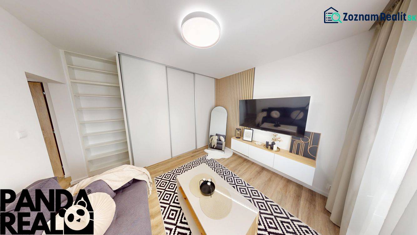 Obývací pokoj v 1-pokojovém bytě s TV, zrcadlem a podlahou s dřevěným dekorem.