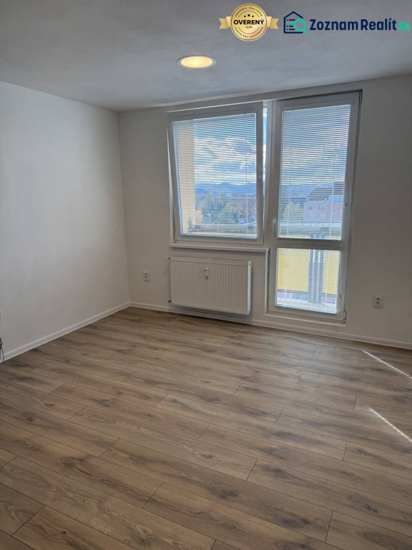 Garsonka s podlahou s dřevěným dekorem a velkým oknem, poskytujícím výhled do okolí.