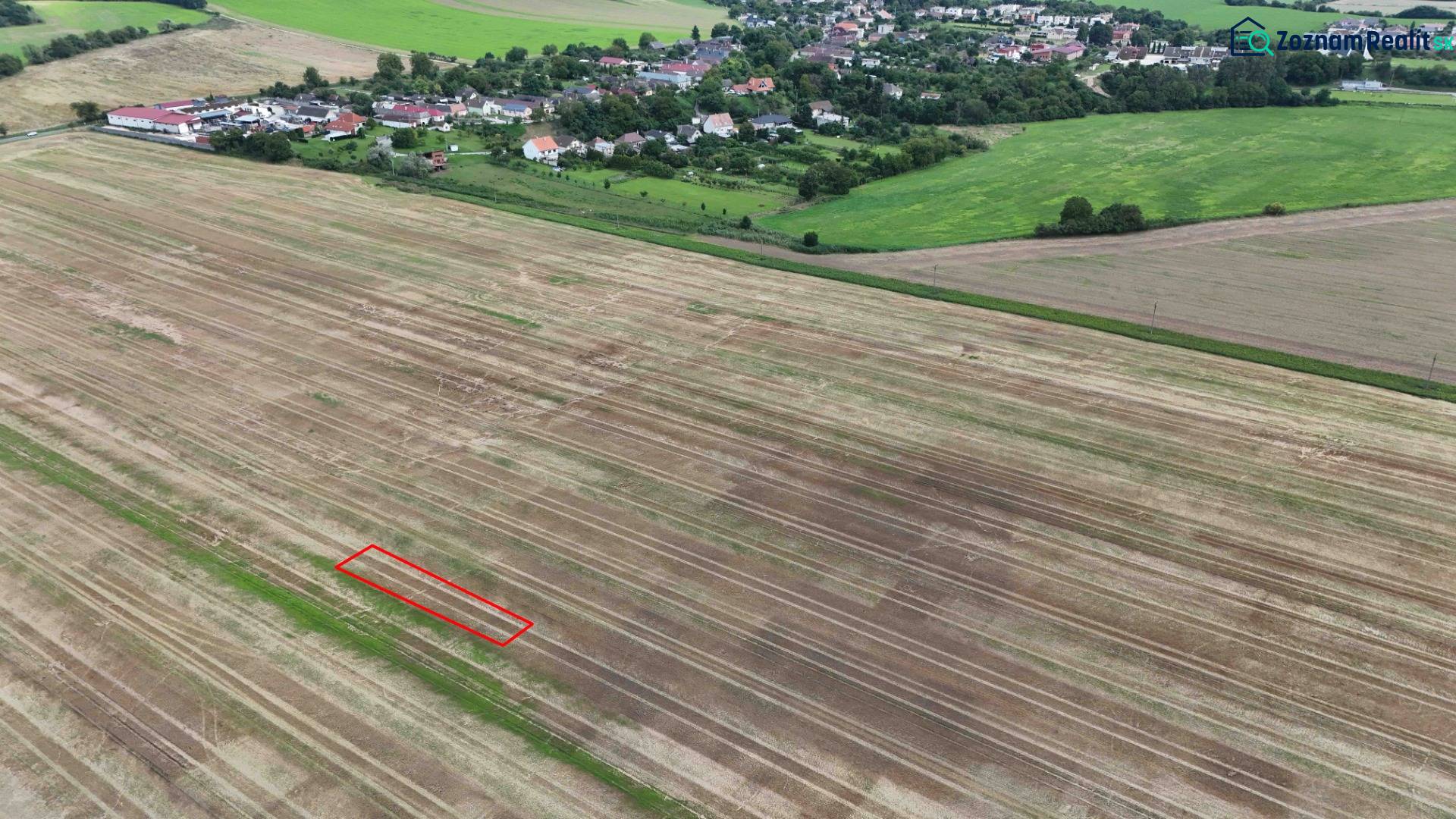 Zemědělské a lesní pozemky u Nové Vsi nad Váhom s vesnicí v pozadí.