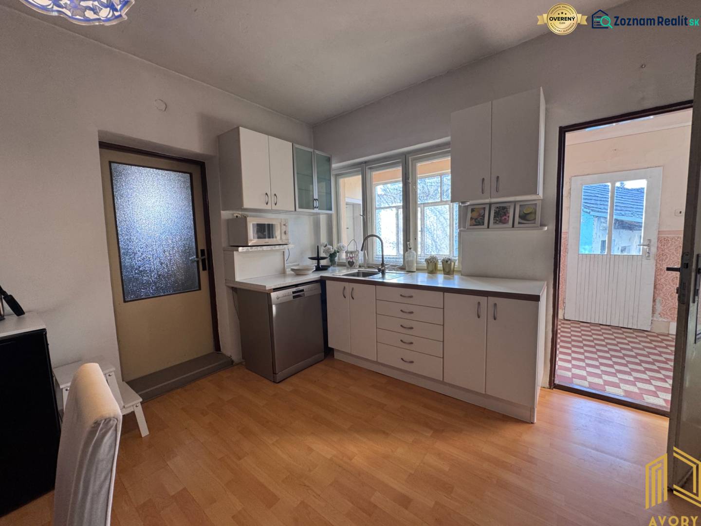 Kuchyně s bílou linkou a podlahou s dřevěným dekorem v rodinném domě.