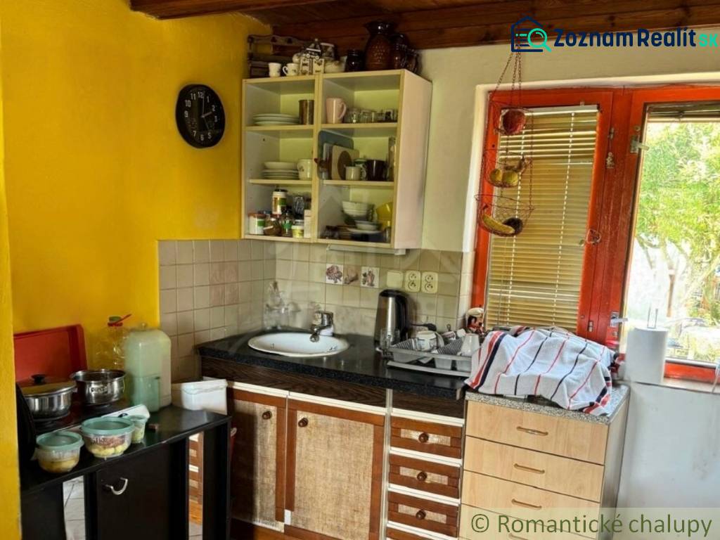 Kuchyně v chatě s dřevěným stropem a žlutou stěnou, vybavená základním nádobím.