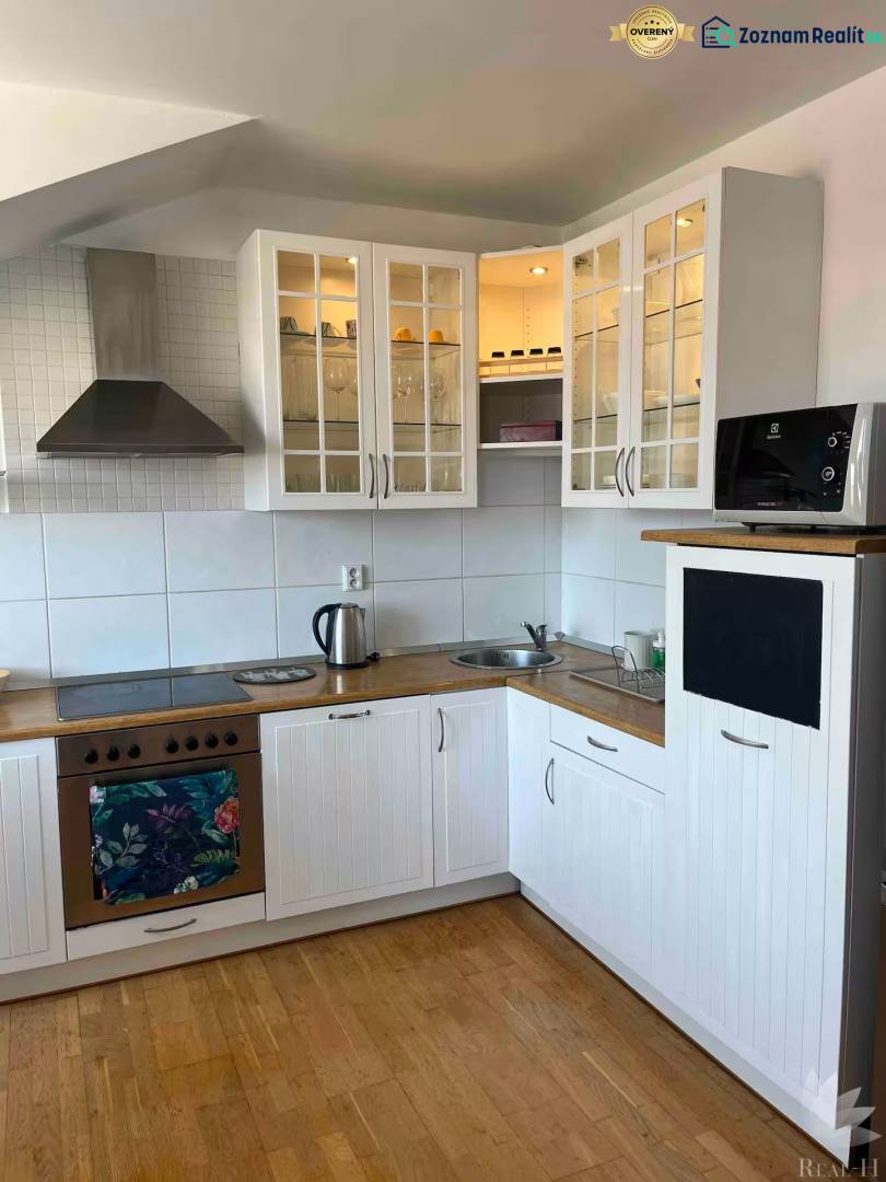 Kuchyně v 3-pokojovém bytě s dřevěnou podlahou, bílými skříňkami a úložným prostorem.