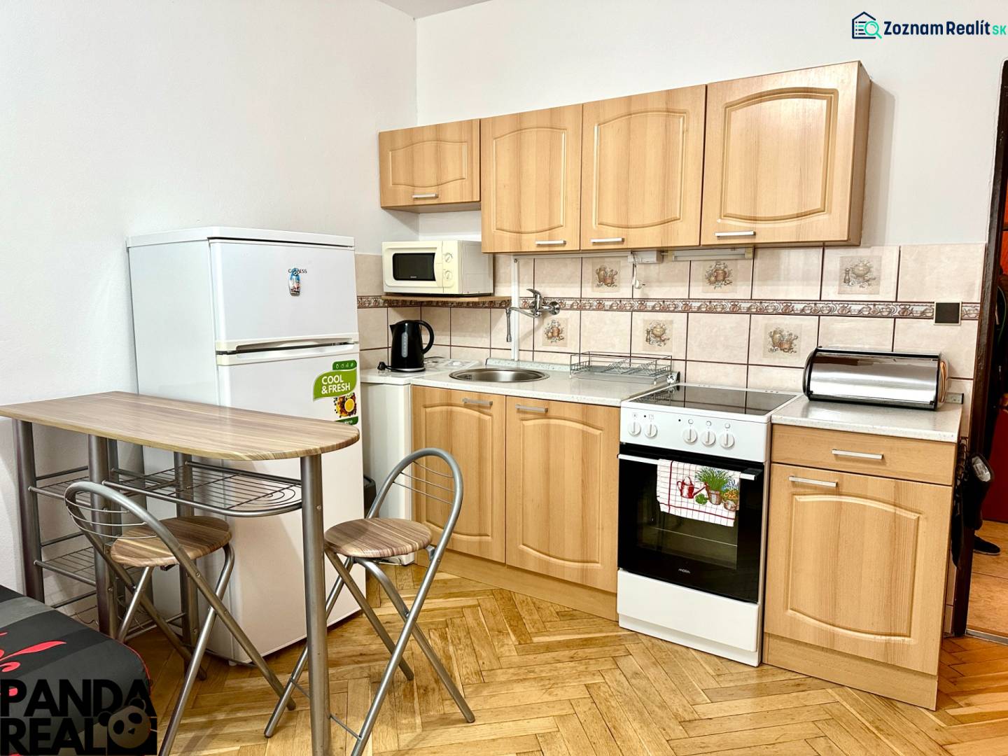 Kuchyně v garsonce s podlahou s dřevěným dekorem, se spotřebiči a sezením.