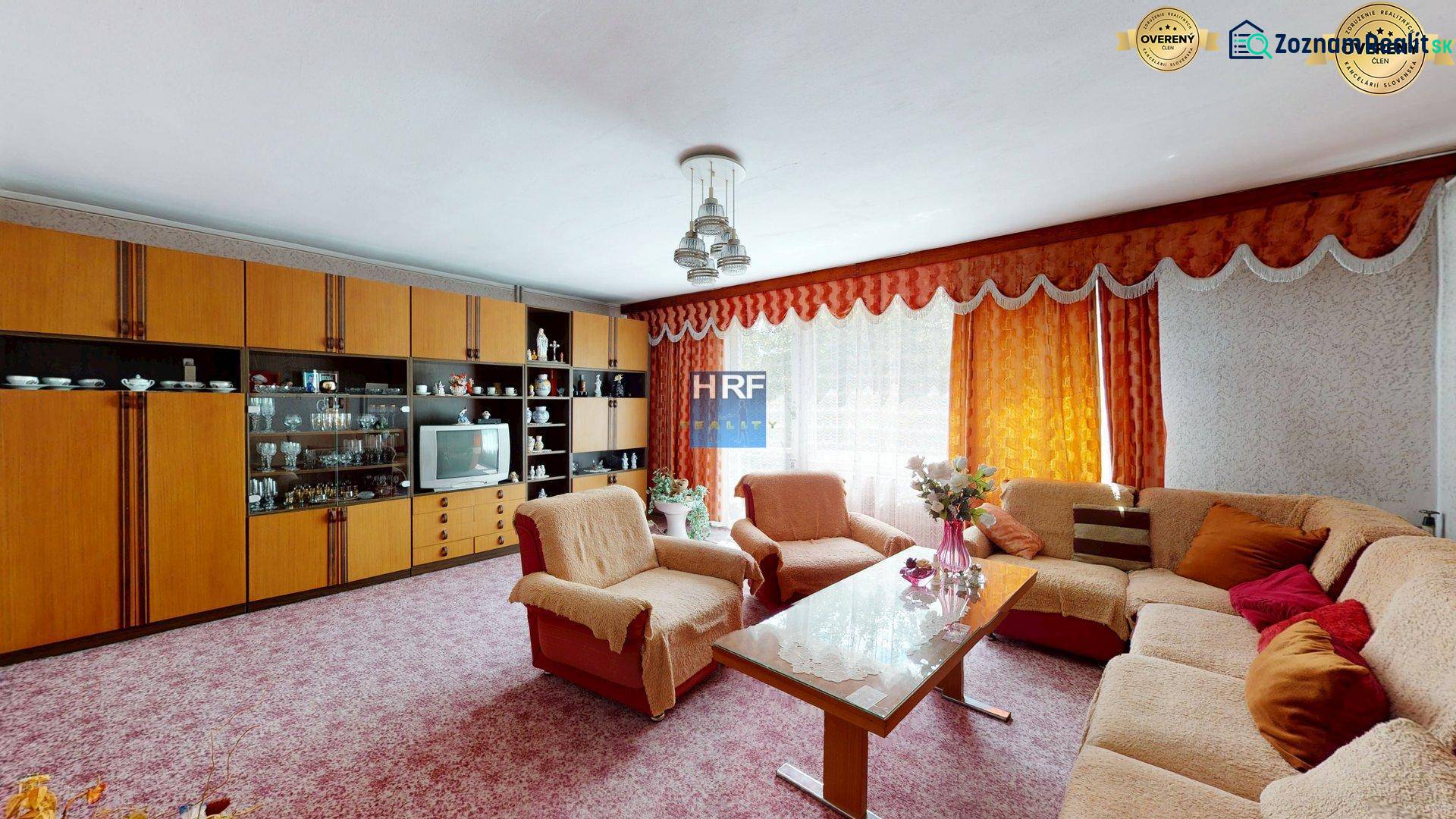 Obývací pokoj v rodinném domě se sedací soupravou, obývací stěnou a květinami.