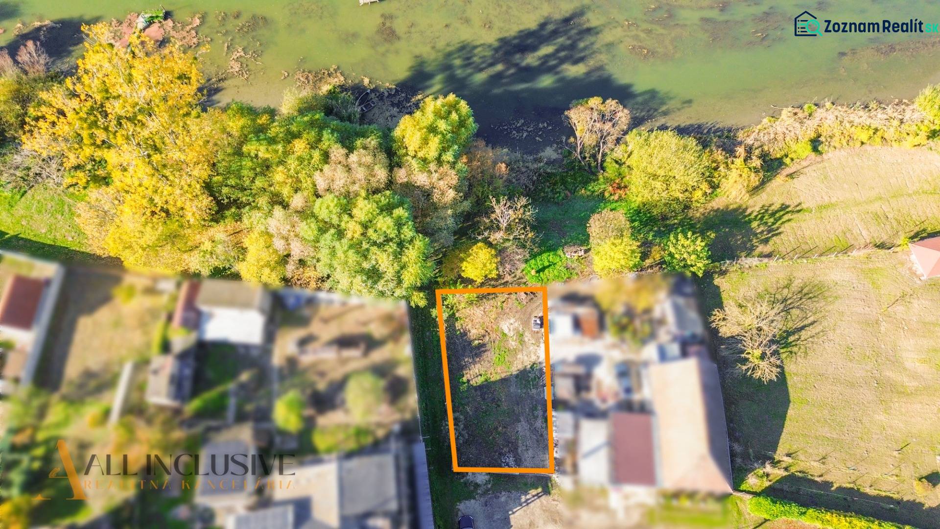 Letecký pohled na pozemek v Jahodné určený k bydlení, obklopený zelení blízko vody.