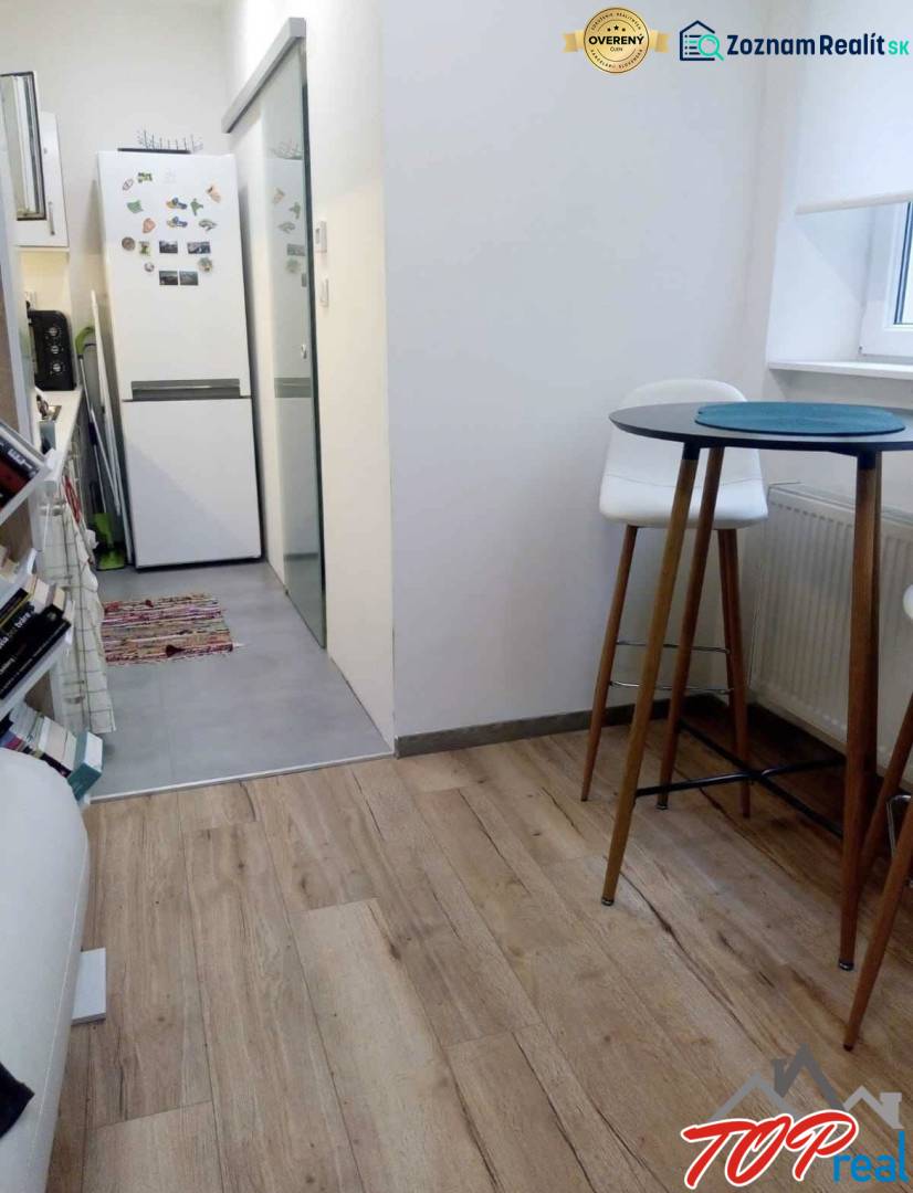 Kuchyně v 1-pokojovém bytě s podlahou s dřevěným dekorem, vysoký stůl a židle.