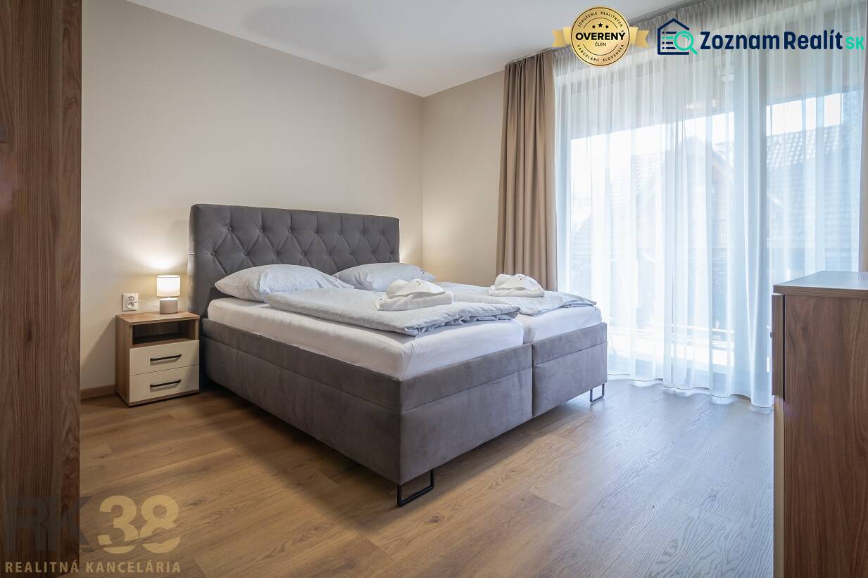 Ložnice v 2pokojovém bytě s velkou postelí a podlahou s dřevěným dekorem.