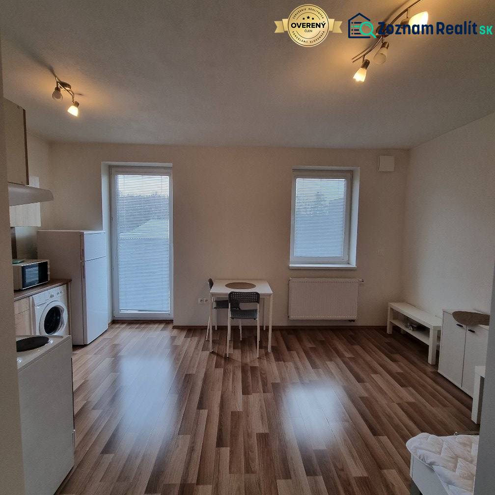 Garsonka s podlahou s dřevěným dekorem, stolem a spotřebiči.