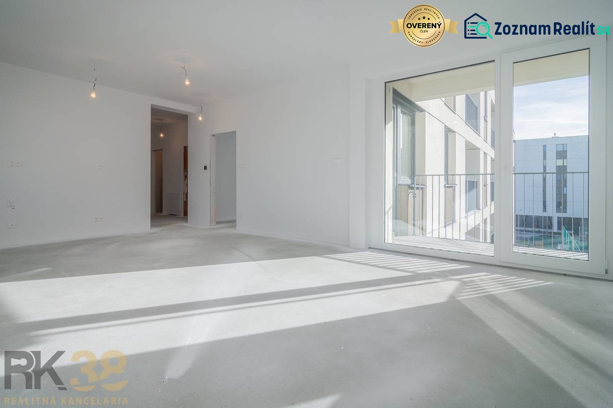 Pokoj v 3-pokojovém bytě s velkým oknem, podlaha s dřevěným dekorem, bílé stěny.