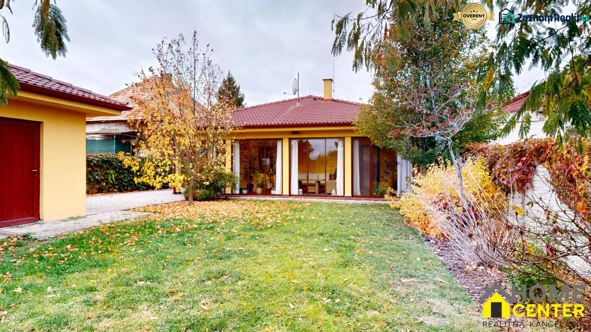 Rodinný dům na Jetelové ulici v Iži se zahradou, listnatými stromy a trávníkem.