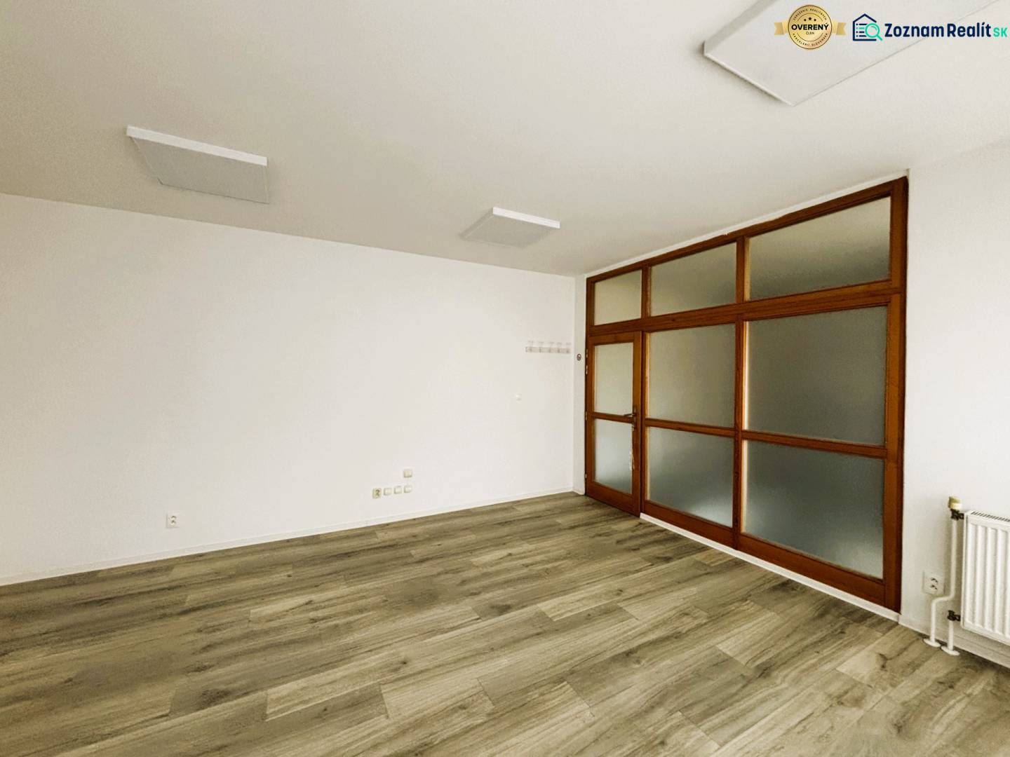 Obchodní prostory s bílými stěnami a podlahou s dřevěným dekorem, prosklené dveře.