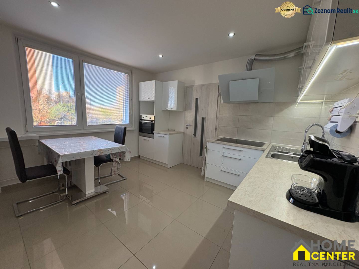 Kuchyně 3pokojového bytu s velkými okny, jídelním stolem a světlou podlahou.