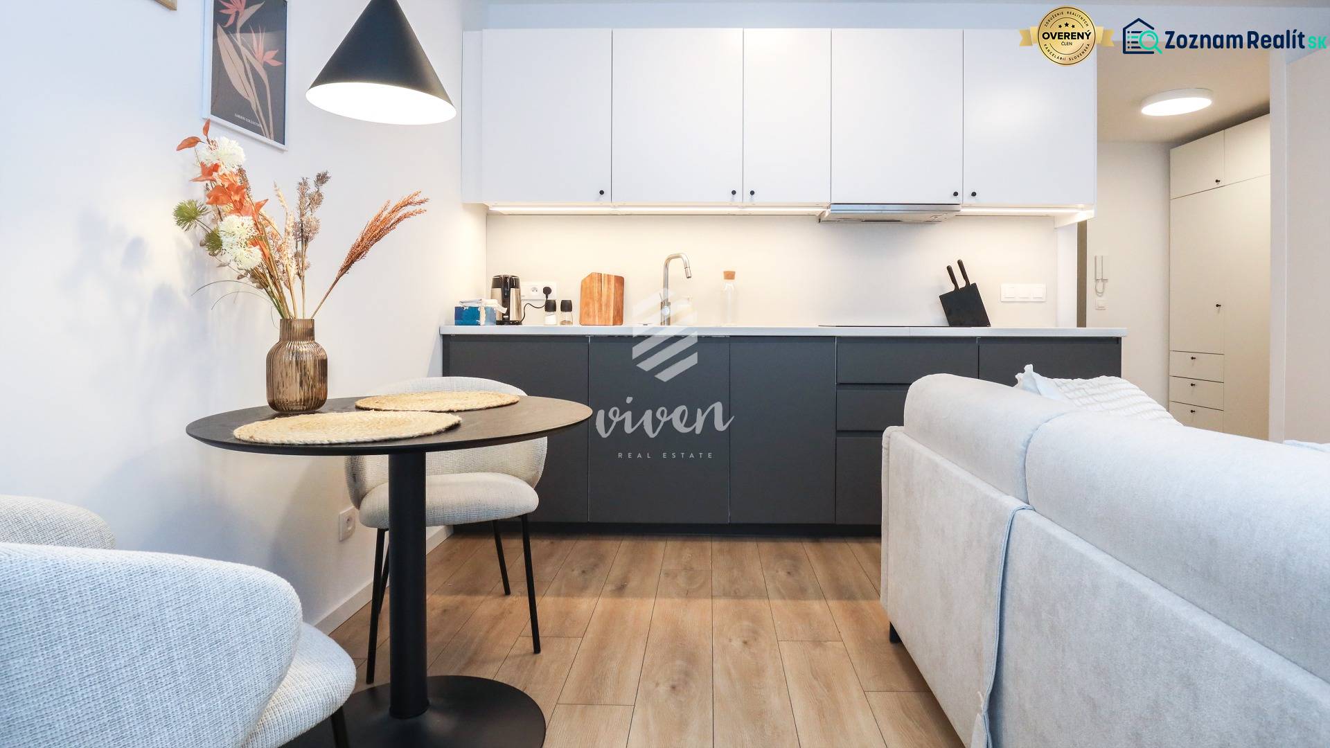 Kuchyně v 1-pokojovém bytě s bílými skříňkami, tmavou linkou a podlahou s dřevěným dekorem.