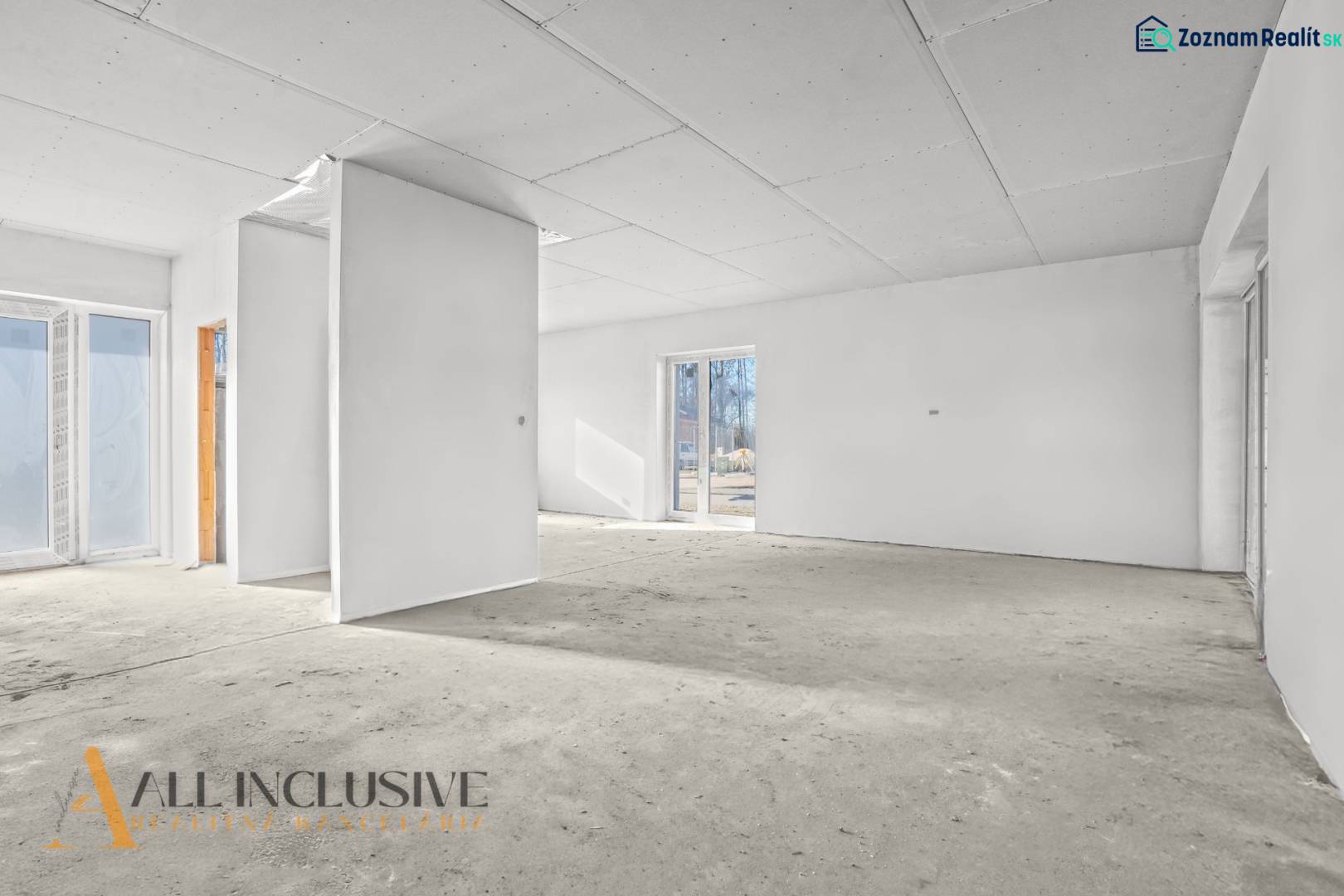 Prázdný interiér v rodinném domě s bílými stěnami a velkými okny.