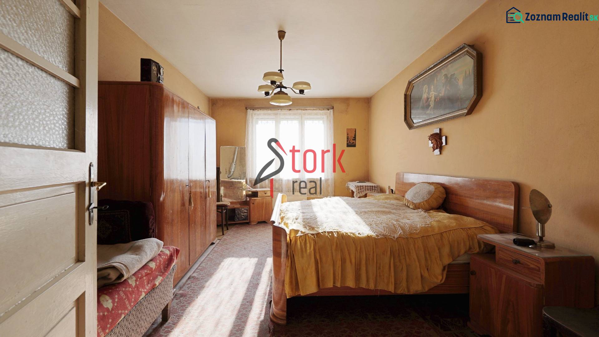 Ložnice v rodinném domě s nábytkem, lustrem a obrazem na stěně.