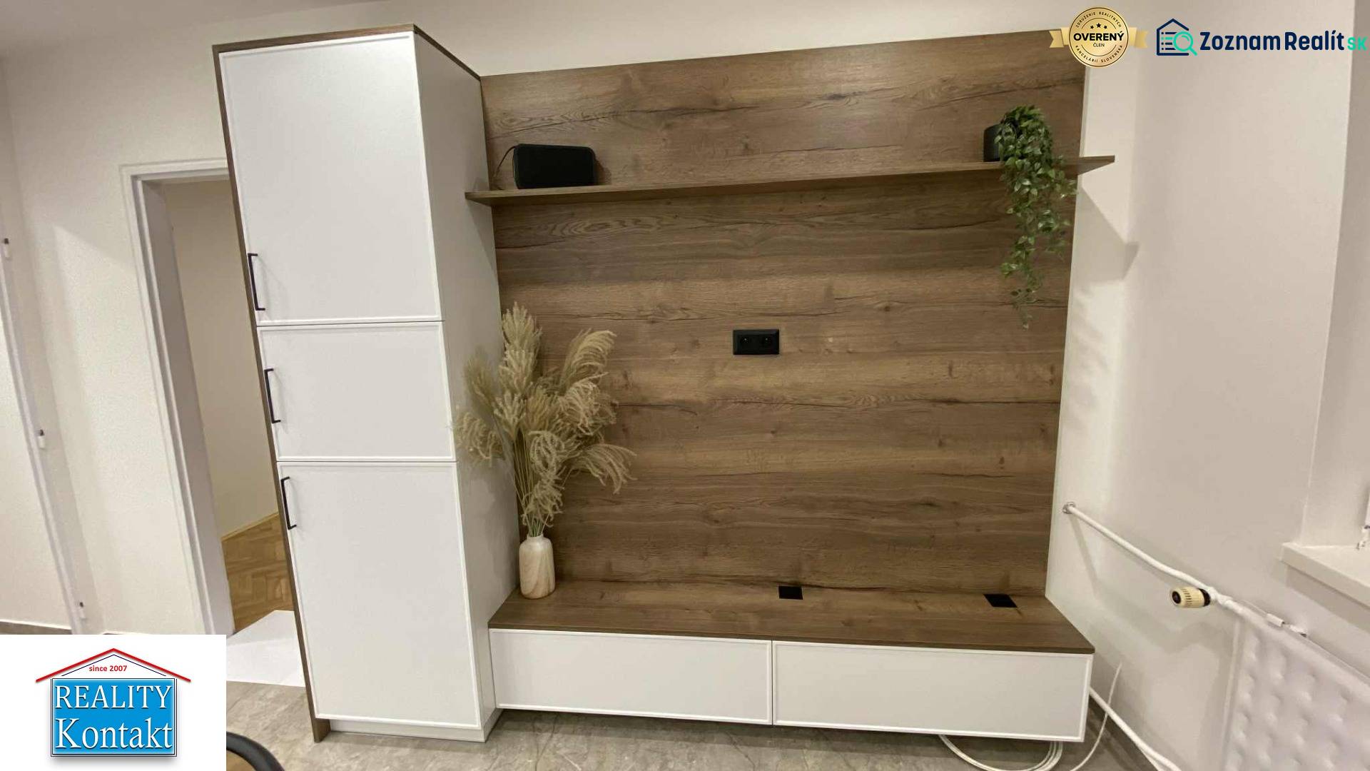 V 1-pokojovém bytě je šatníková stěna s dřevěným dekorem a květinami ve váze.