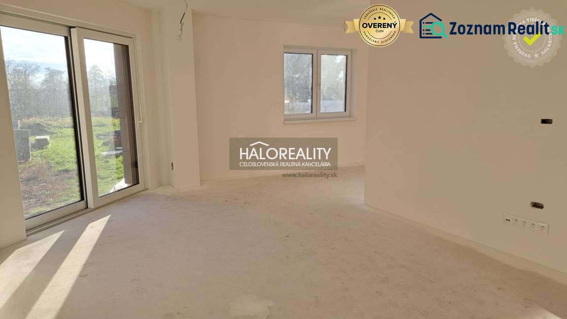 Interiér rodinného domu s velkým oknem, bílými stěnami a terasovými dveřmi.