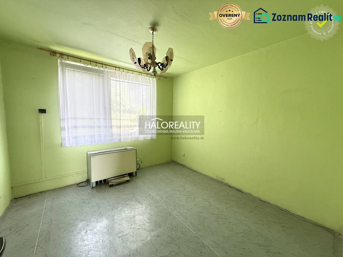 Pokoj s lustrem, oknem a topným tělesem v 3-pokojovém bytě.