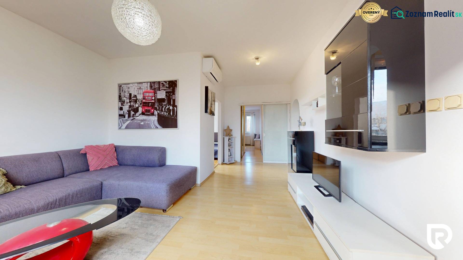 Obývací pokoj v 3pokojovém bytě s pohovkou, TV sestavou a podlahou s dřevěným dekorem.