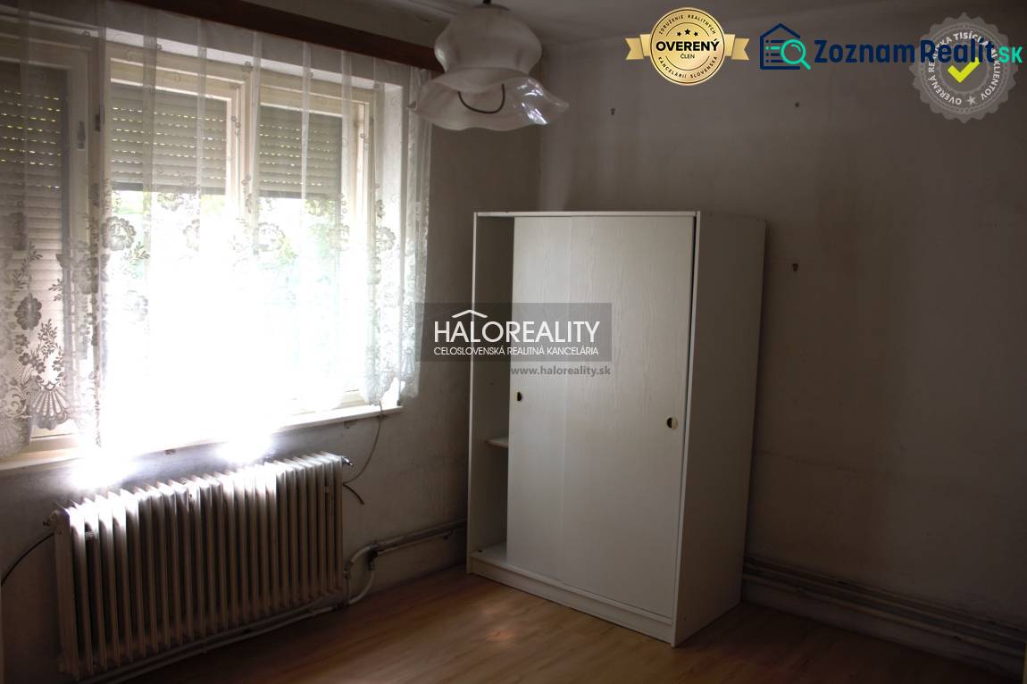 Pokoj v rodinném domě s velkým oknem, radiátorem a bílou skříní.