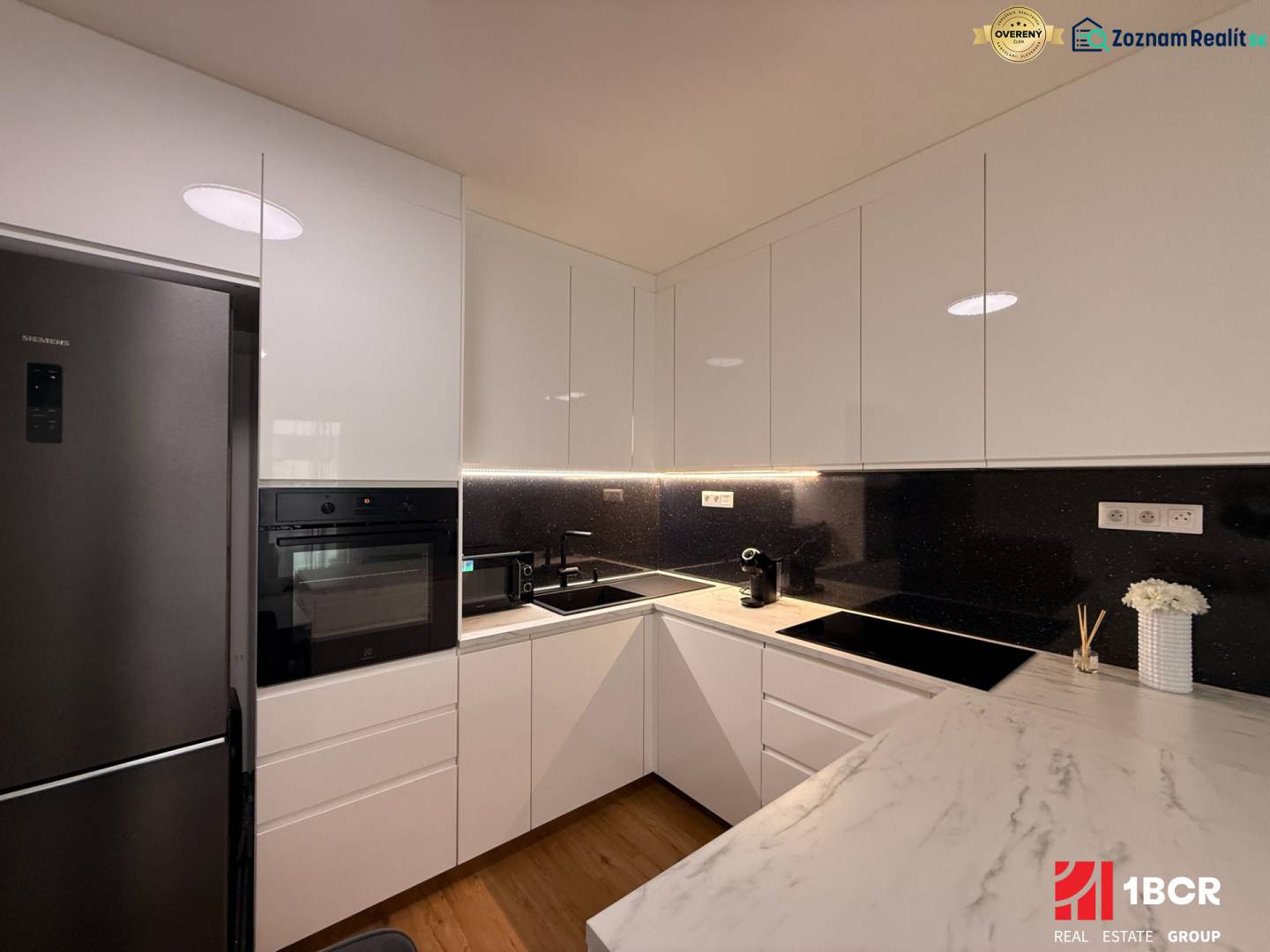 Kuchyně v 2-pokojovém bytě s lesklou bílou linkou a podlahou s dřevěným dekorem.