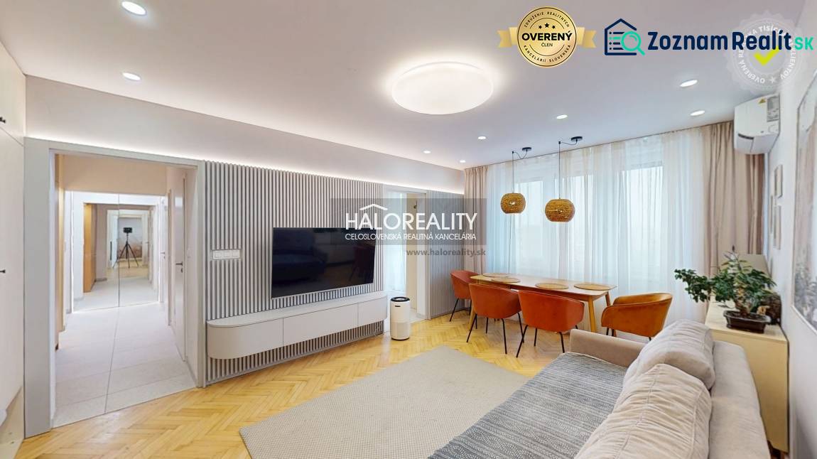 Obývací pokoj v 3-pokojovém bytě s TV na stěně, sedačkou a jídelním stolem.