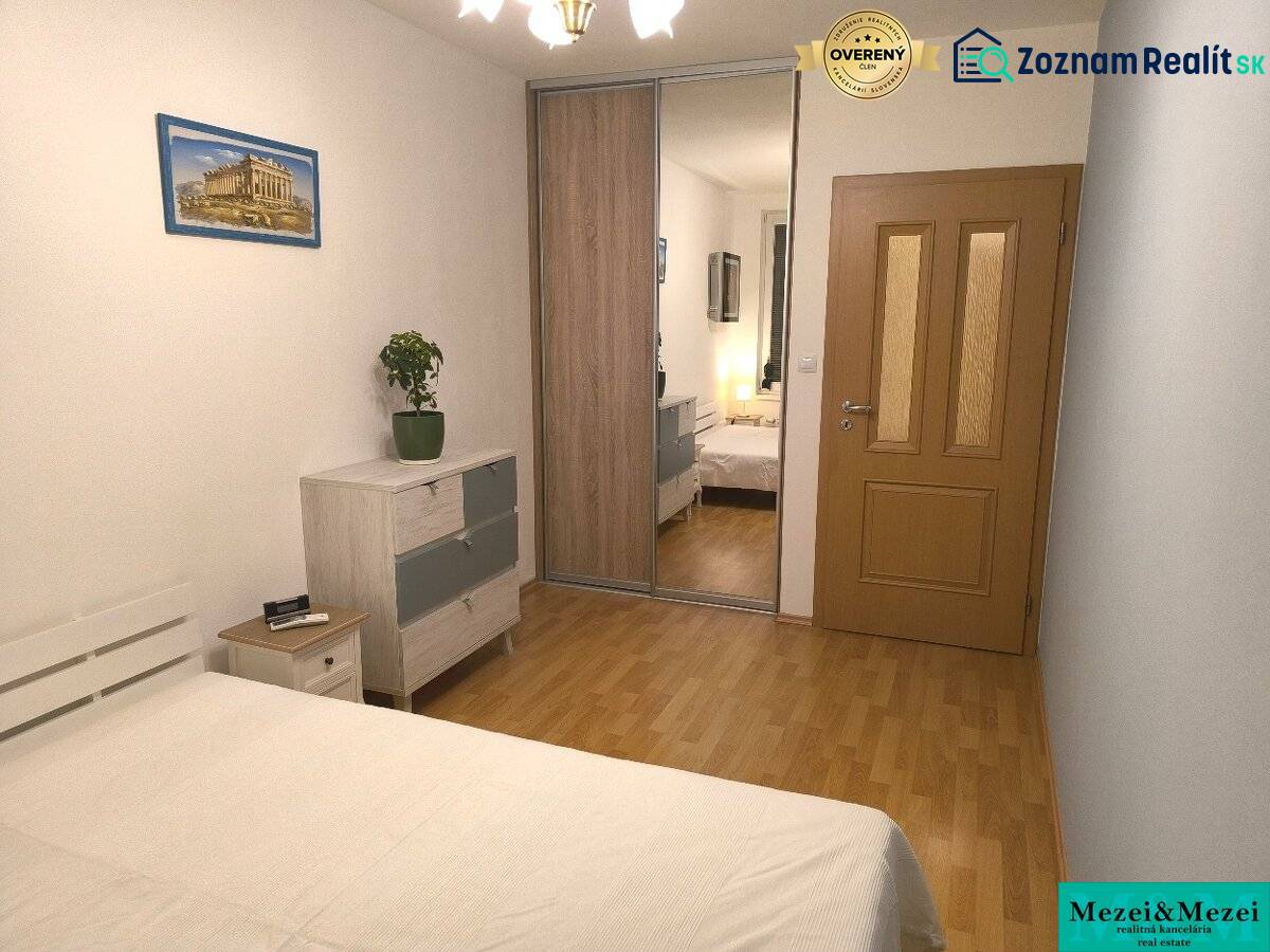 Ložnice v 2-pokojovém bytě s podlahou s dřevěným dekorem, skříně se zrcadlem a obrazem.