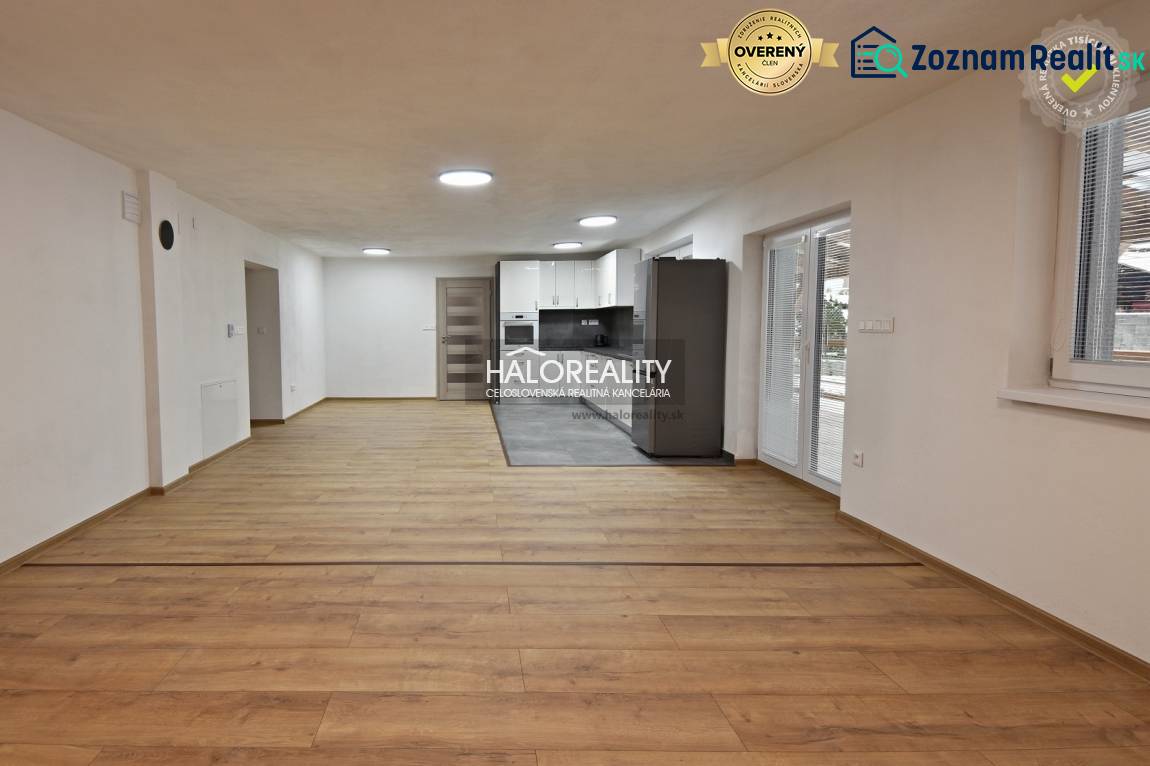 Obývací pokoj v rodinném domě s kuchyní, podlaha s dřevěným dekorem, bílé stěny.