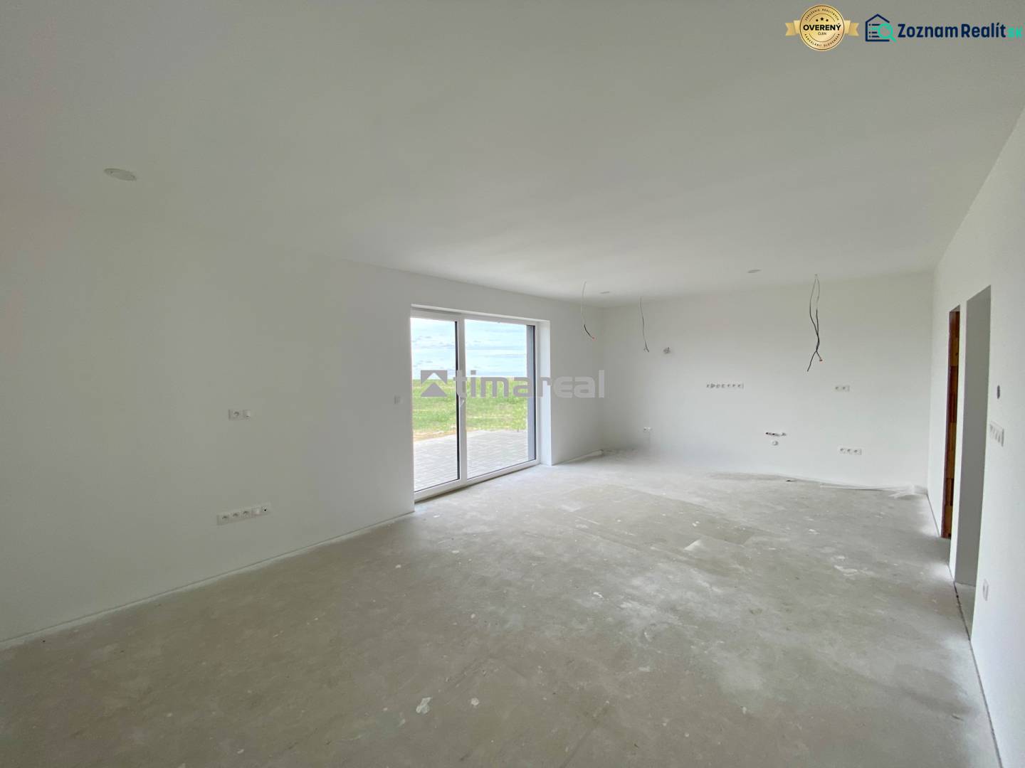 Prostorná místnost s velkými skleněnými dveřmi a výhledem na zahradu v rodinném domě.