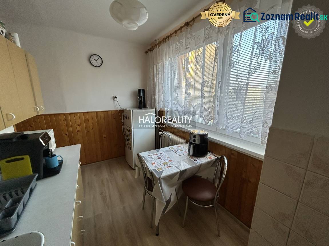 Kuchyně s dřevěným dekorem v 2pokojovém bytě. Jemné záclony, jídelní stůl, kávovar.