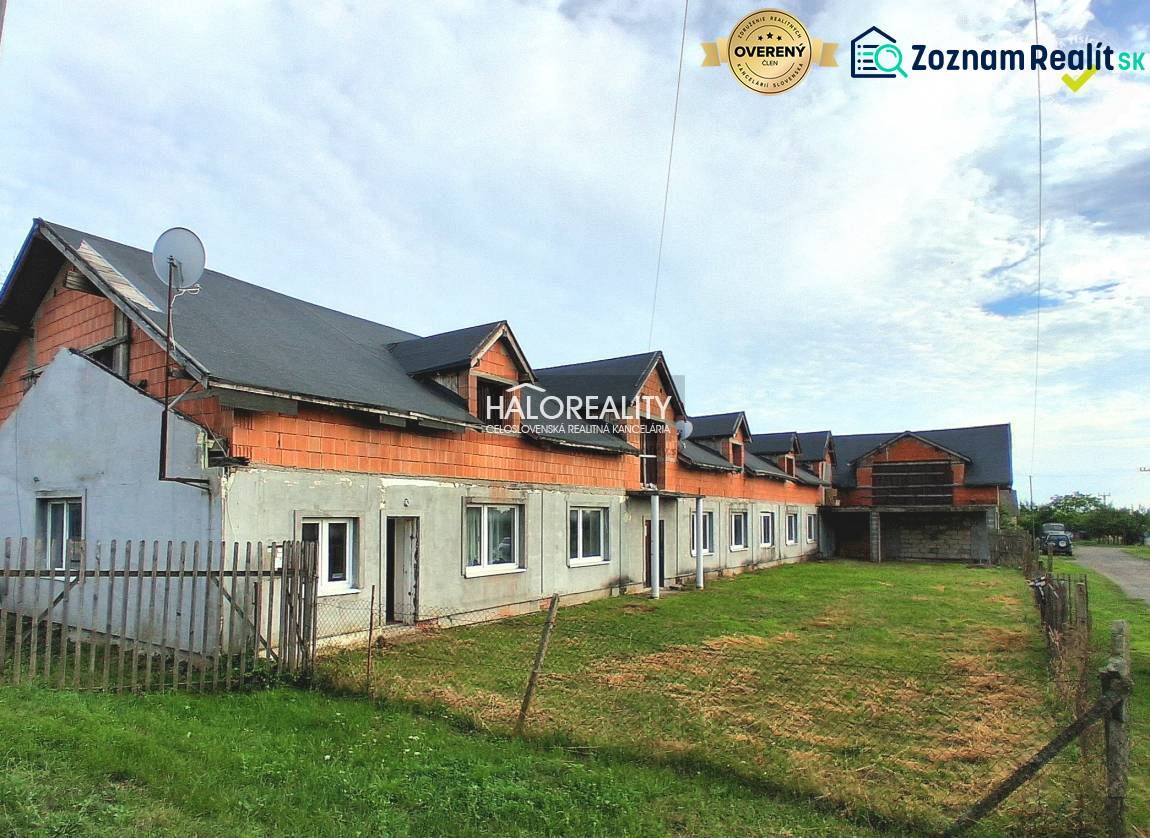 Obchodní prostory v Tibavě, nedokončená budova s travnatým prostorem a plotem.