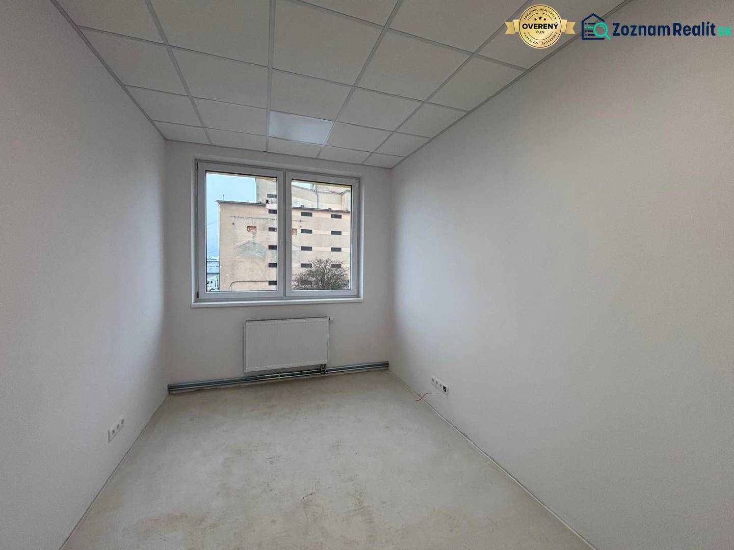 Bílá kancelář s radiátorem a výhledem z okna.