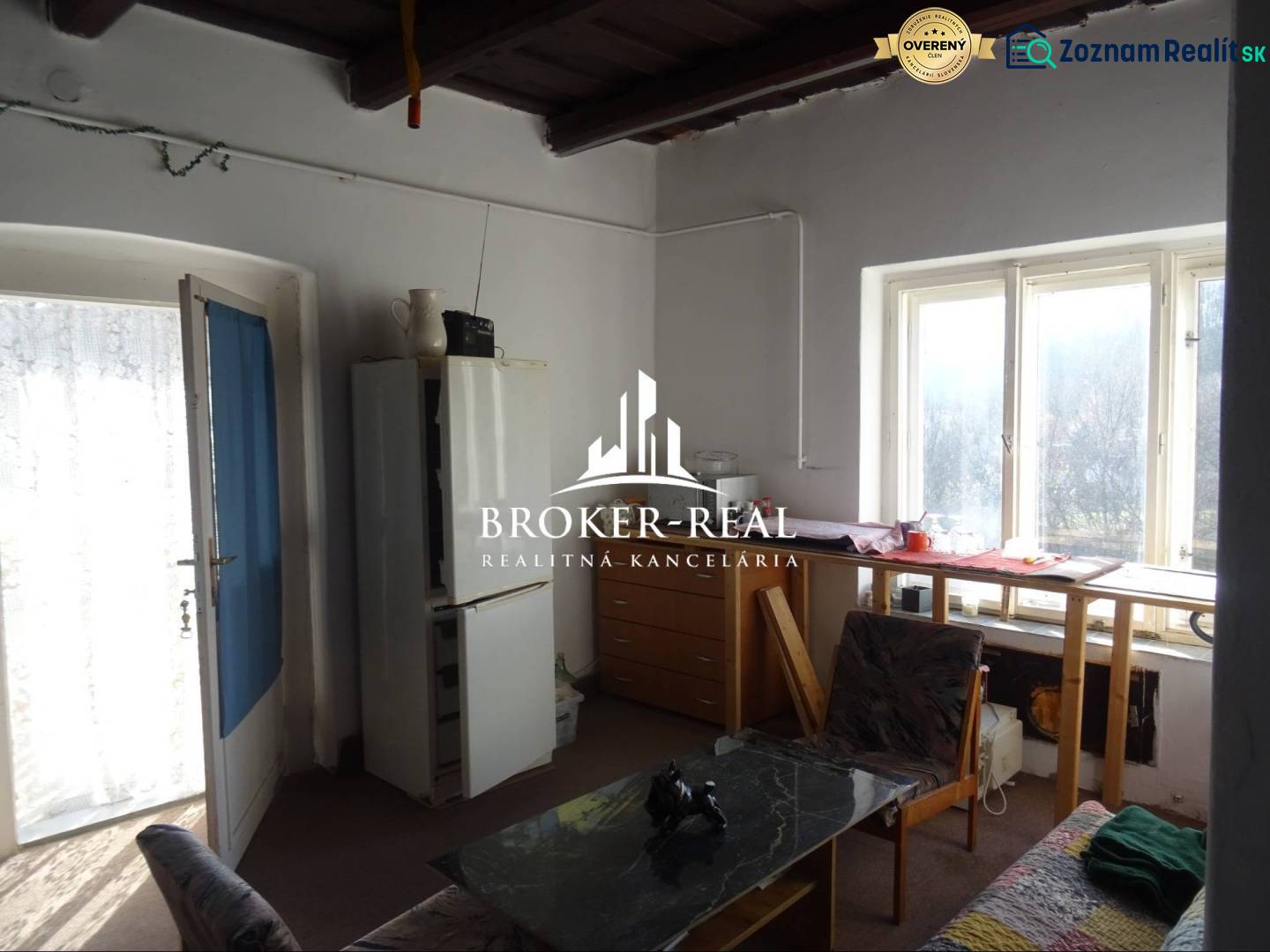 Pokoj v rodinném domě s prosvětleným stolem u okna, křeslem a jídelním stolem.