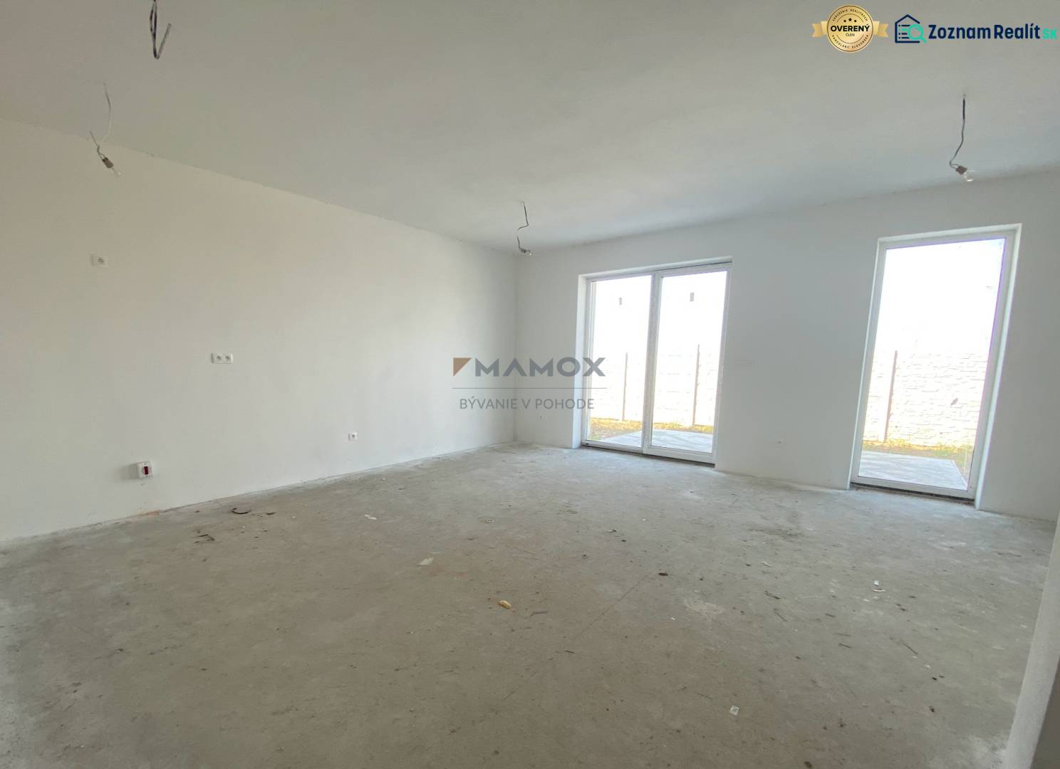 Prostorný pokoj v rodinném domě s betonovou podlahou a velkými okny.