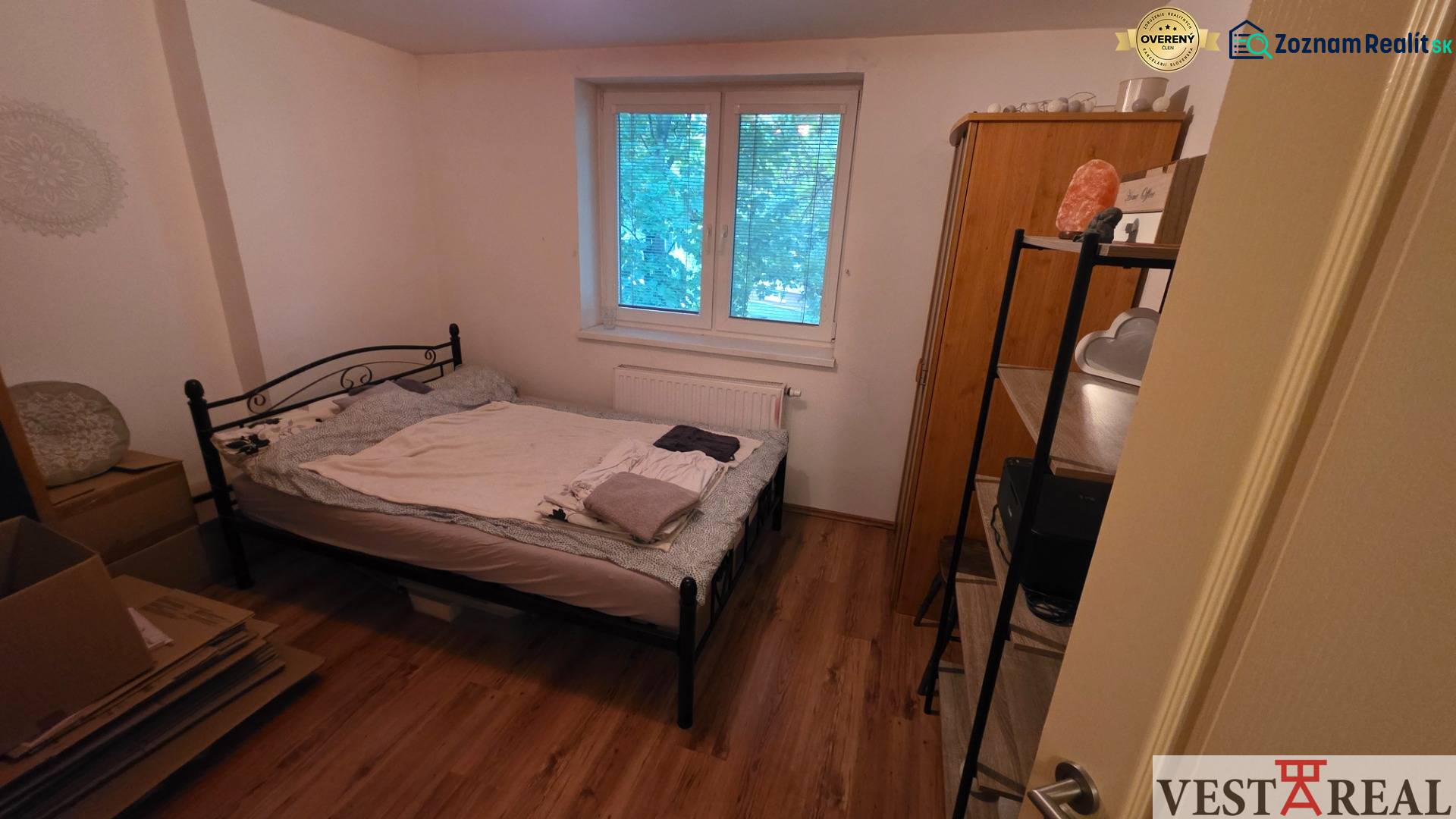 Ložnice ve 3-pokojovém bytě s kovovou postelí a podlahou s dřevěným dekorem.