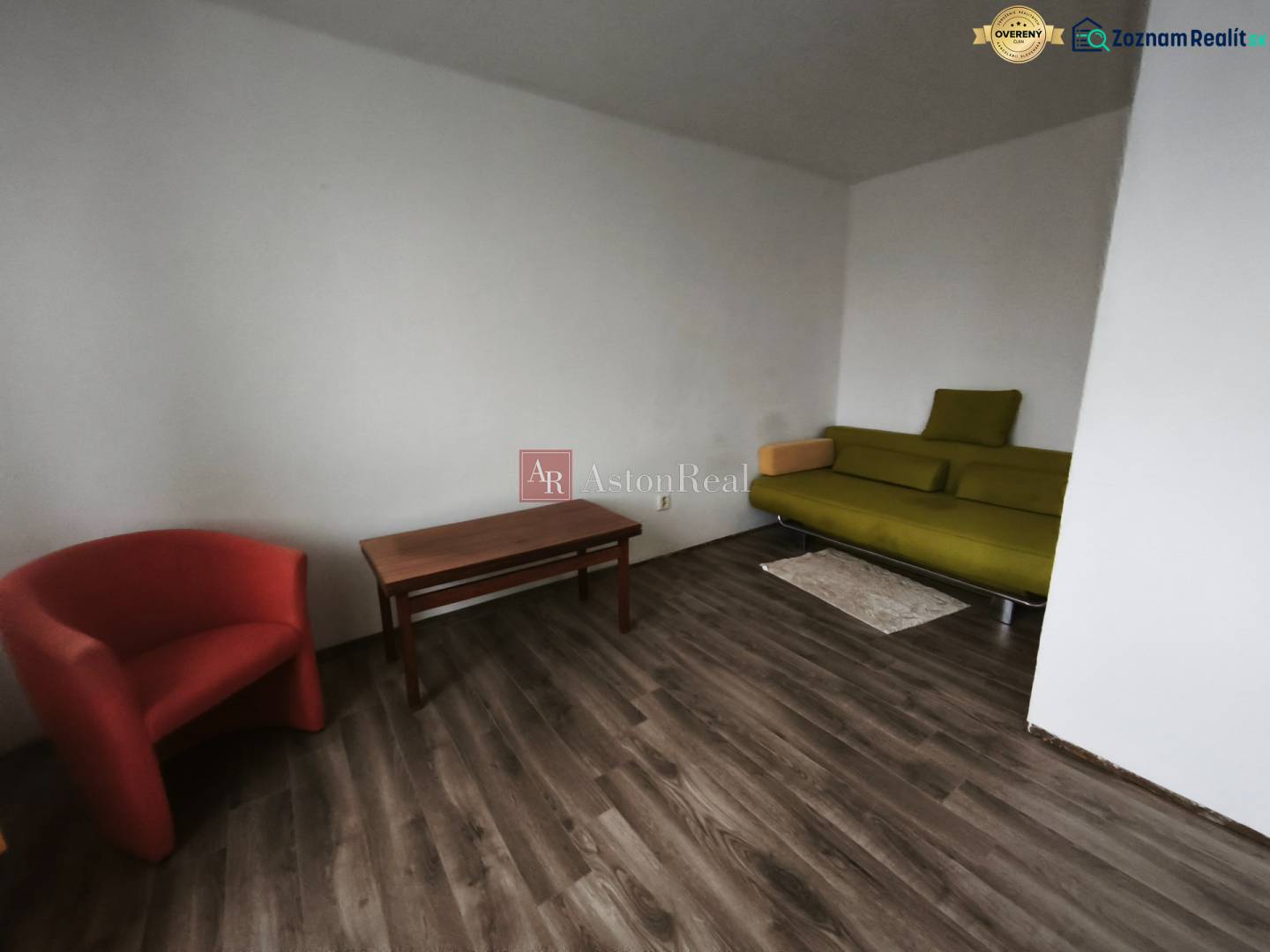 1-pokojový byt s podlahou s dřevěným dekorem, zelenou pohovkou a červeným křeslem.