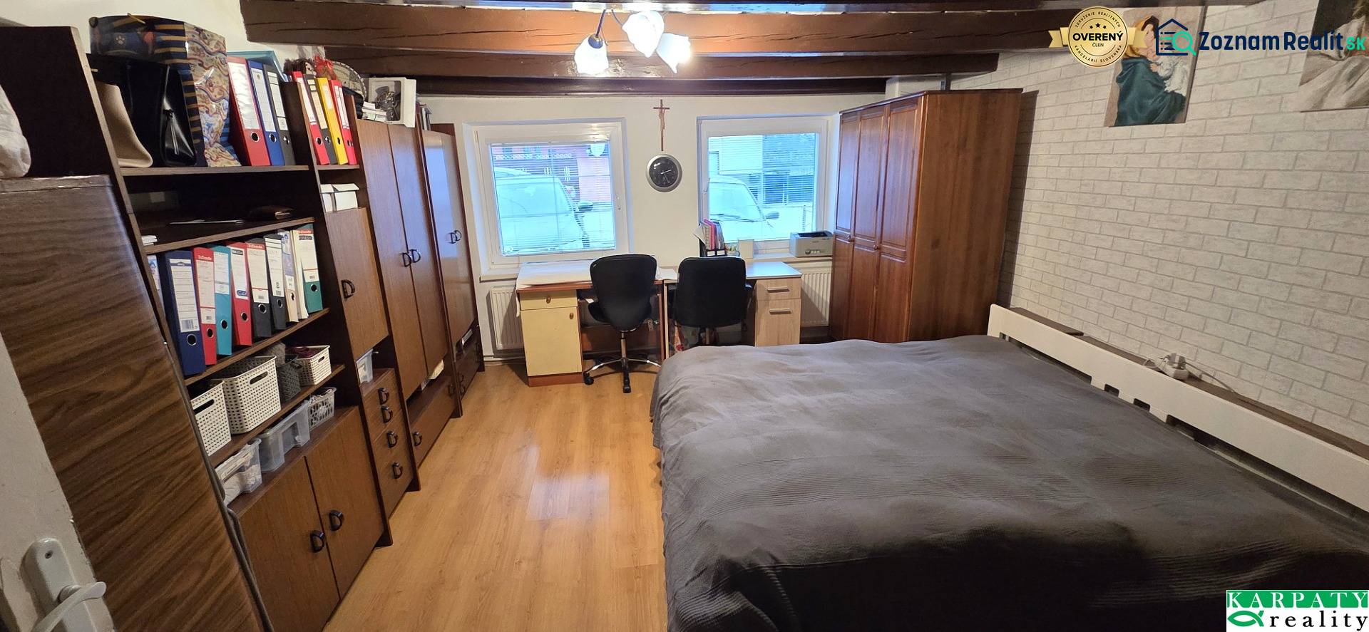 Pokoj v rodinném domě s podlahou s dřevěným dekorem, postelí a kancelářským koutem.
