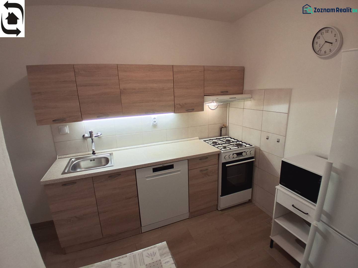 Kuchyně ve 3-pokojovém bytě s linkou, sporákem, myčkou a podlahou s dřevěným dekorem.