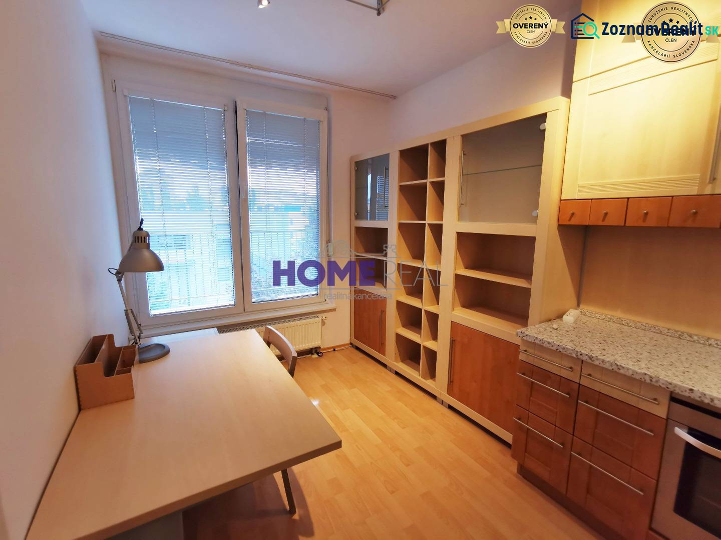Pracovna v 2-pokojovém bytě s podlahou s dřevěným dekorem, stolem a knihovnou.