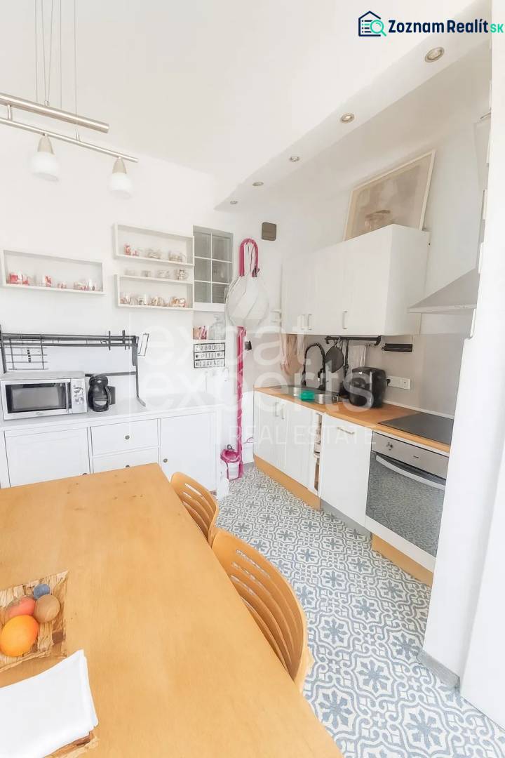 Kuchyně ve 3-pokojovém bytě s jídelním stolem, vzorovanou podlahou a bílými skříňkami.