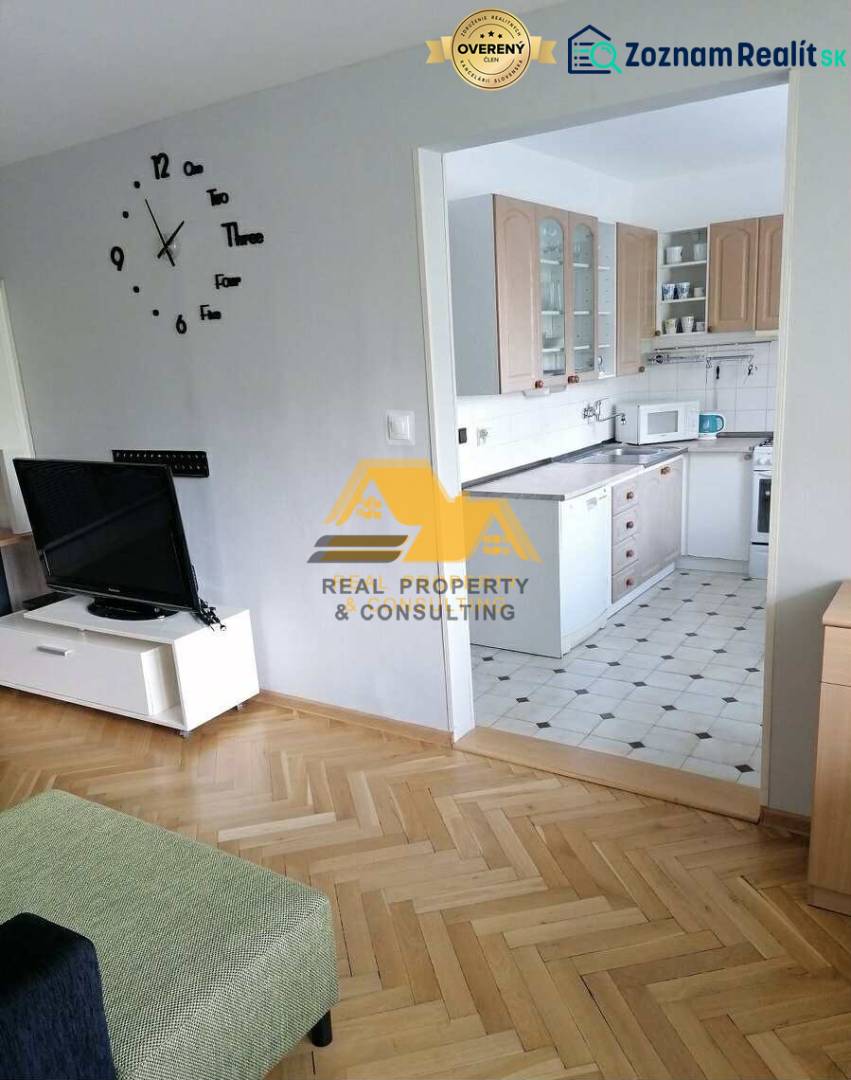 Obývací pokoj v 3-pokojovém bytě s podlahou s dřevěným dekorem a kuchyní v pozadí.