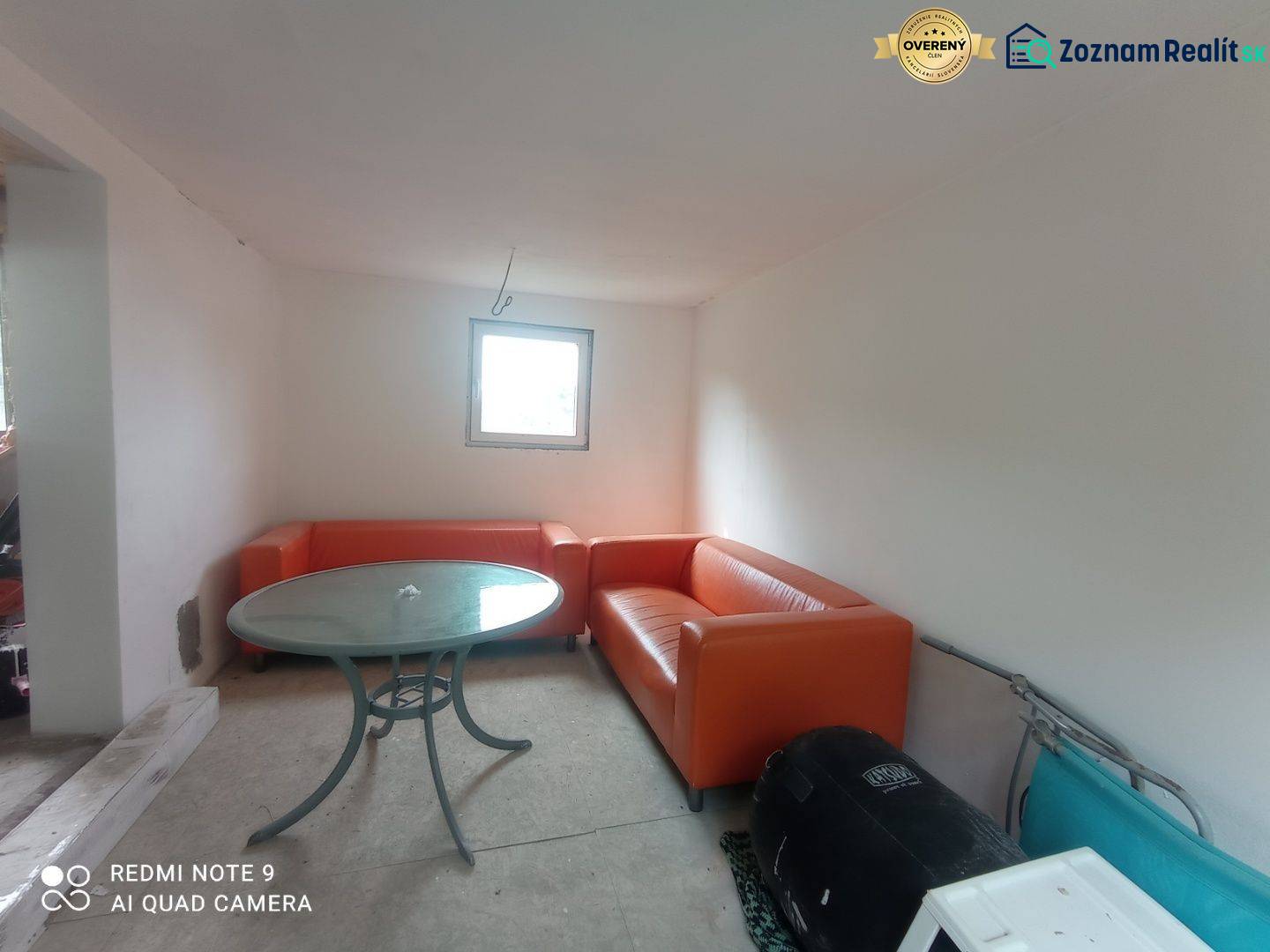 Oranžové sedačky a kulatý stůl doplňují prostor v chatě s bílými stěnami.