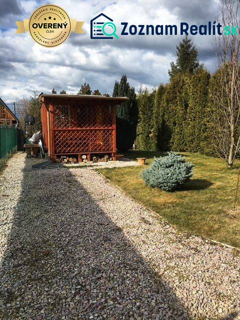 Dřevěná chata v Kráľovej nad Váhom s upravenou zahradou a keřem.